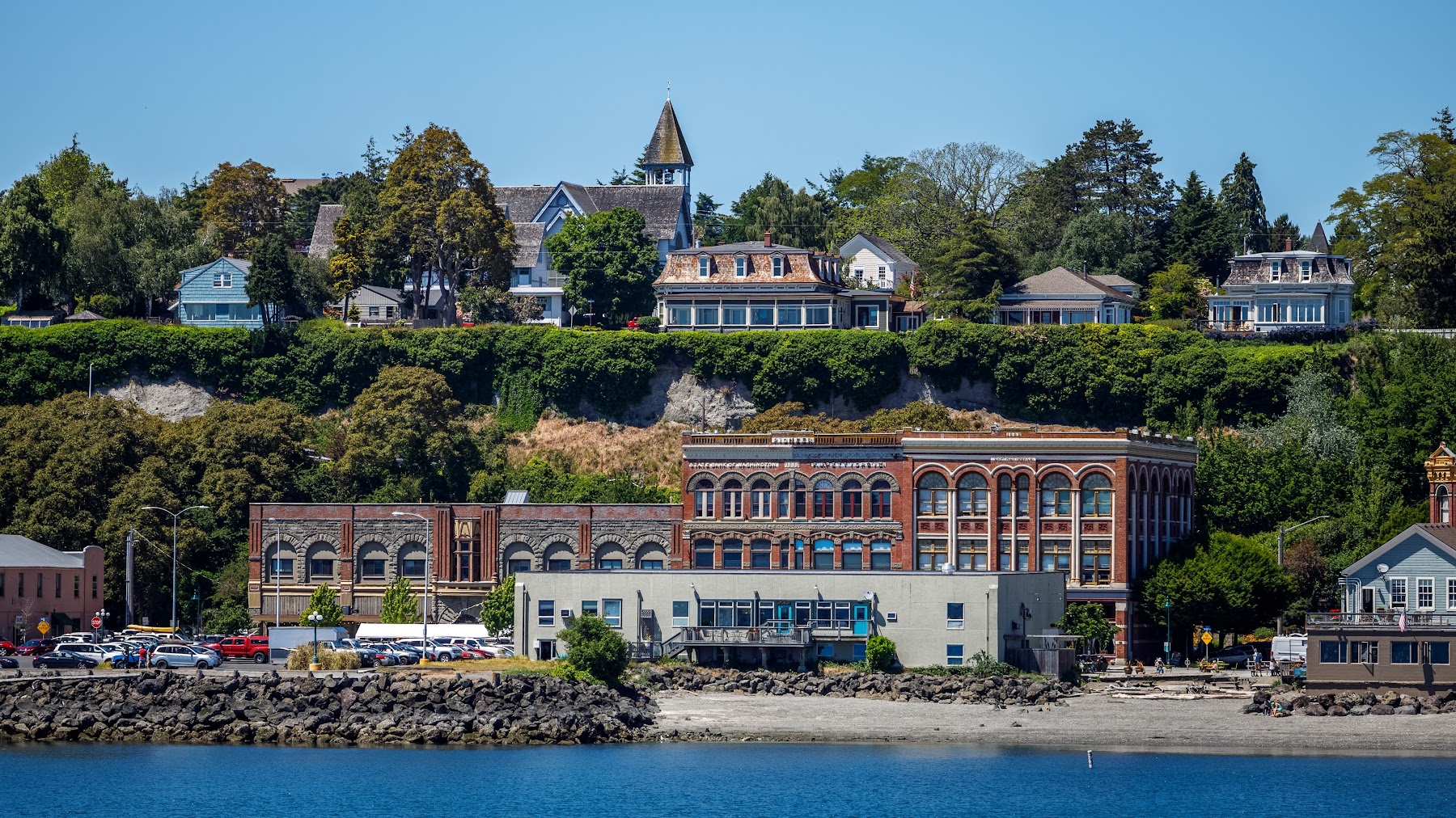 A sailboat glides on the water with the historic Port Townsend waterfront in the background.
