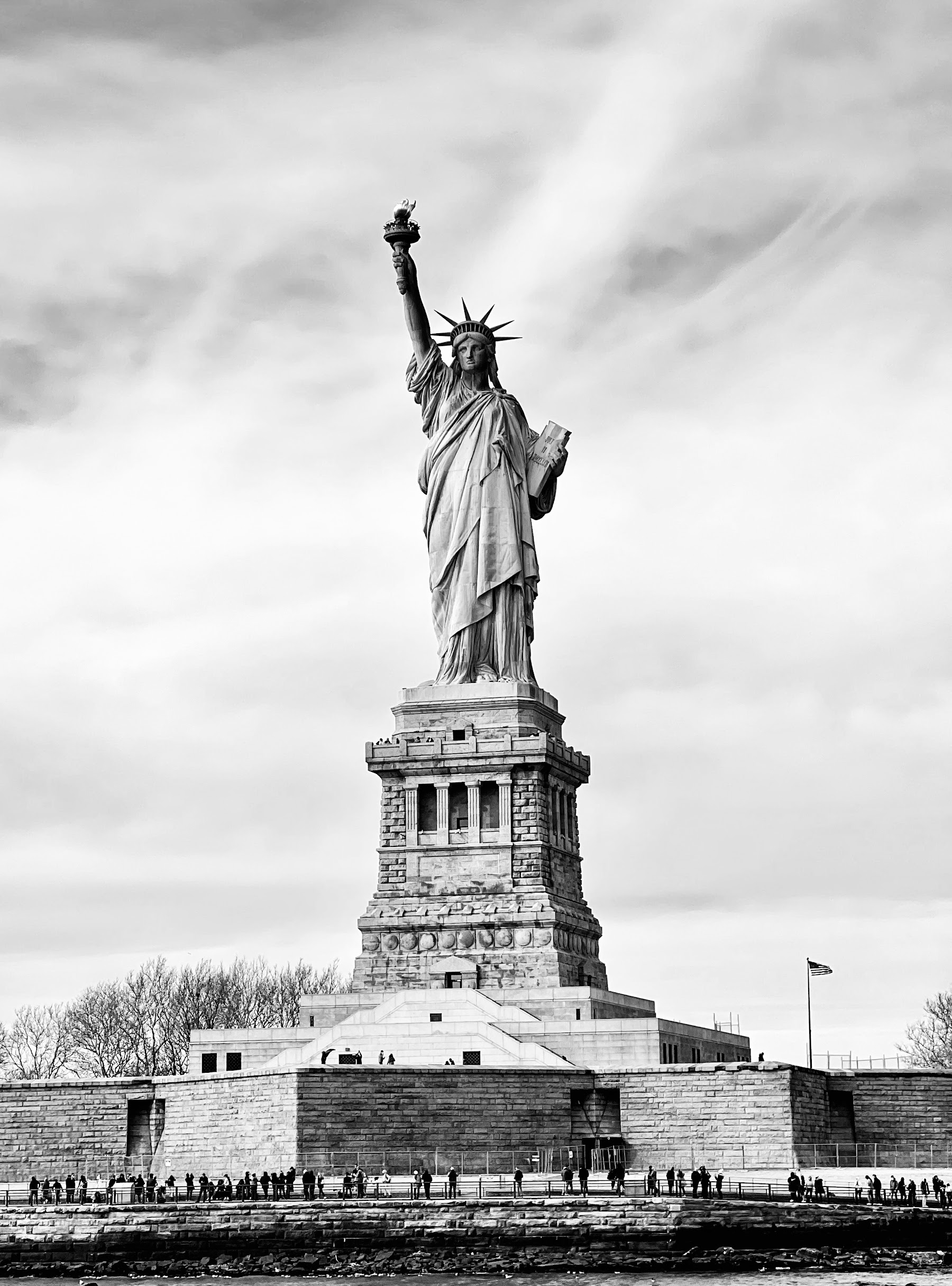 The Statue of Liberty viewed from a ferry on the water, with the New York City skyline in the background.